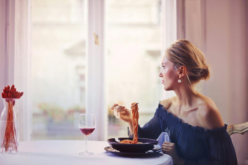 women eating pasta, side view photograph, wine on table